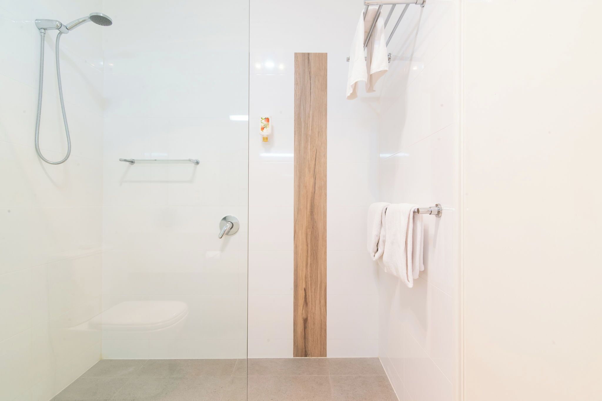 A modern bathroom with a glass-enclosed shower, a wooden accent wall, and a toilet.