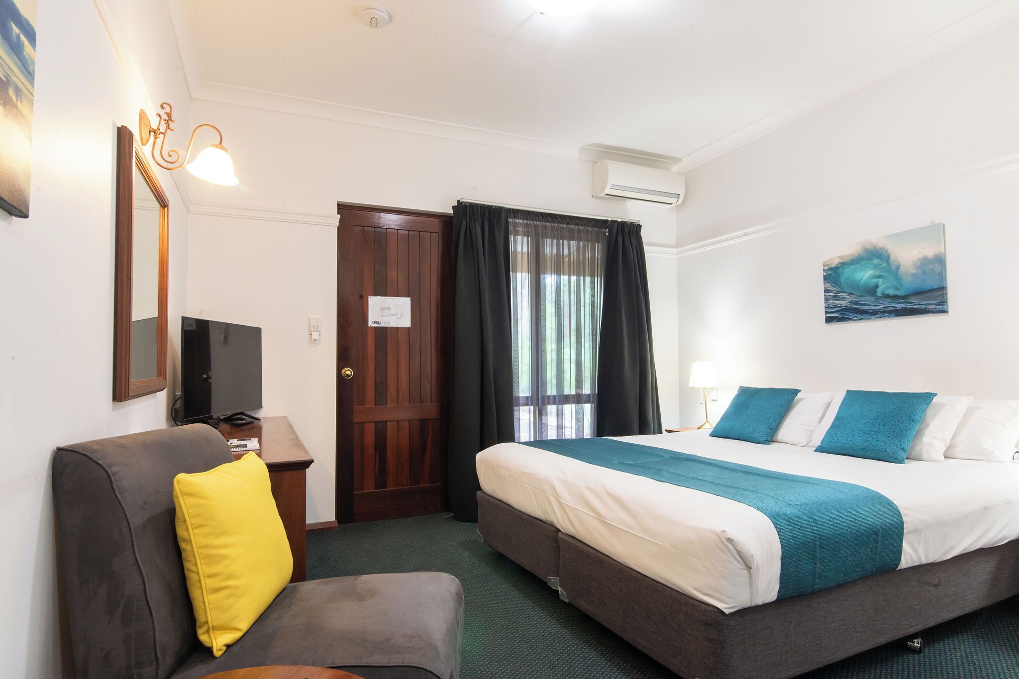 Habitación de hotel con cama, sofá, televisor, espejo y un cuadro en la pared.