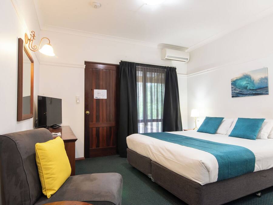 Habitación de hotel con cama, sofá, televisor, espejo y un cuadro en la pared.