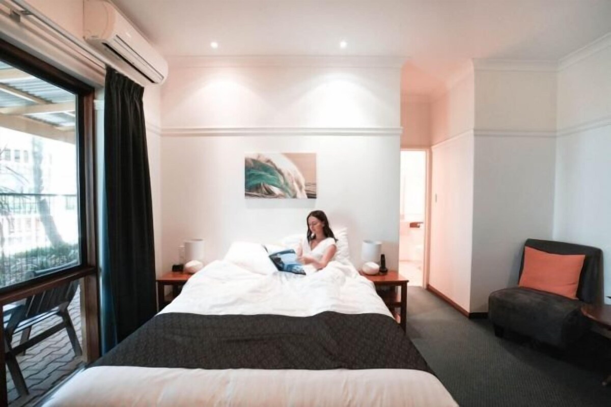 Habitación de hotel con cama, mesita de noche, una silla, ventana con cortinas y aire acondicionado de pared.