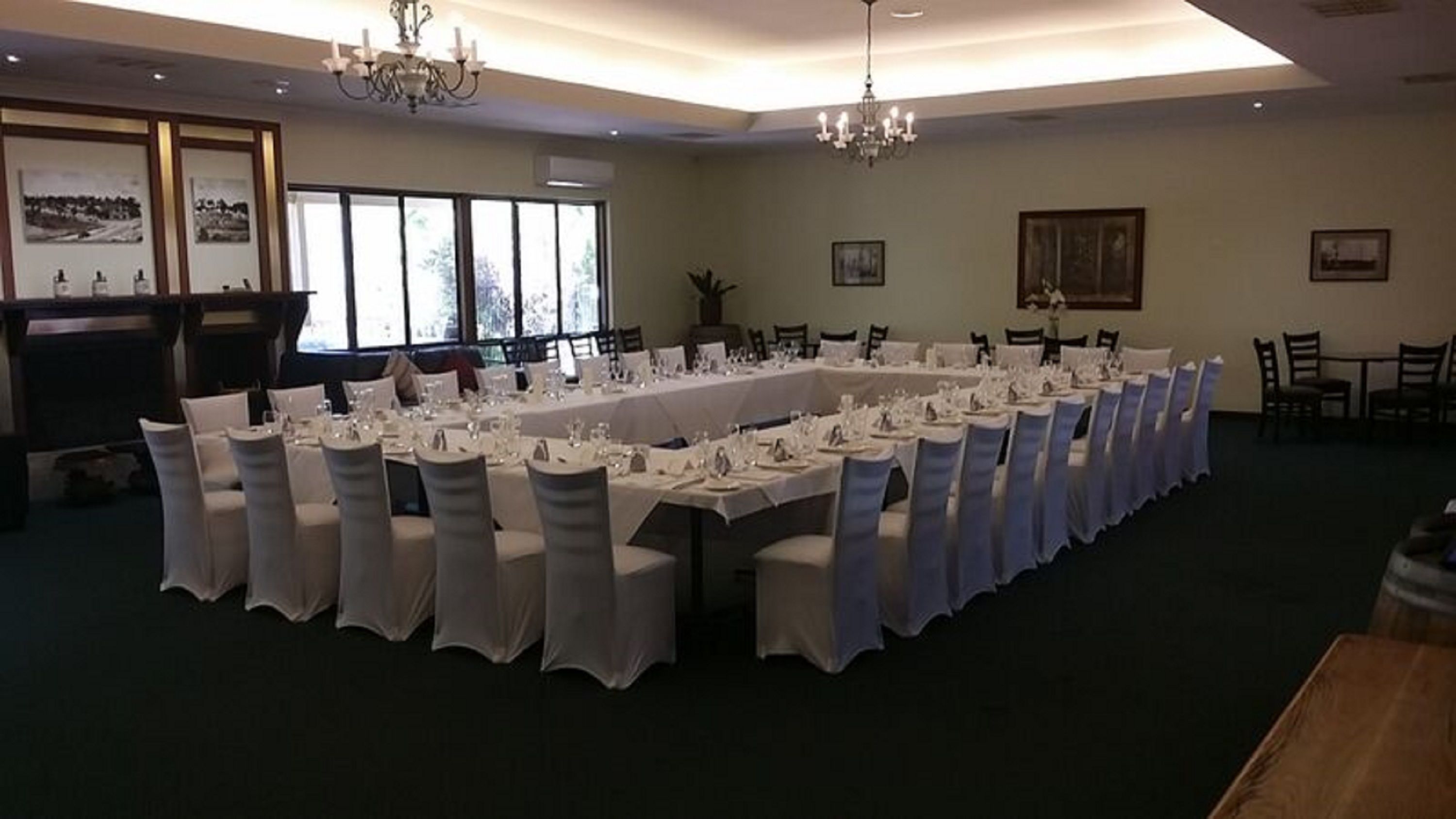 Un salón de banquetes con largas mesas dispuestas para un evento formal, ventanas amplias y candelabros.