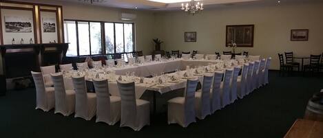 Un salón de banquetes con largas mesas dispuestas para un evento formal, ventanas amplias y candelabros.