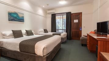 Habitación de hotel con dos camas, un escritorio con televisor, un ventanal con cortinas y un cuadro en la pared.