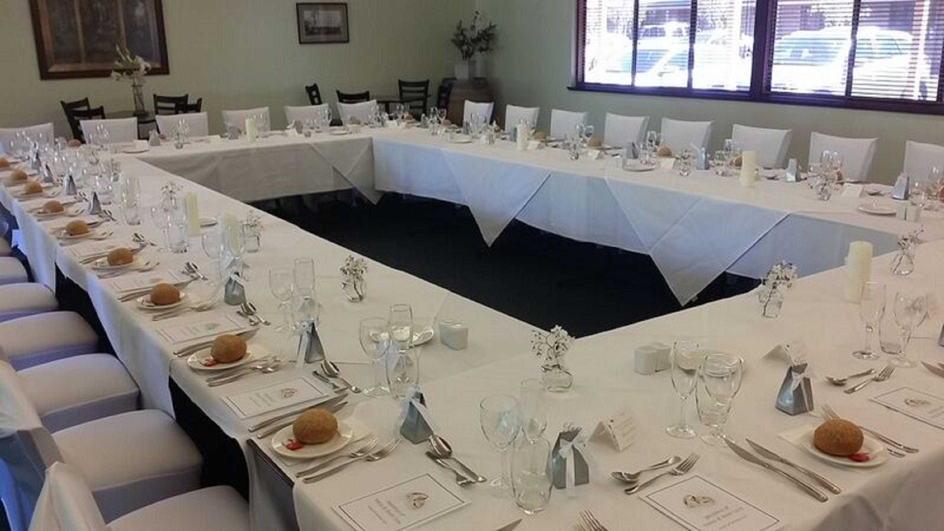 A long dining table set for a formal event with white tablecloths, silverware, and glassware.