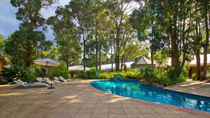 Une piscine dotée d’une terrasse carrelée, entourée d’une végétation luxuriante et d’arbres.