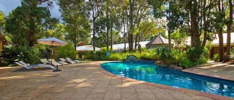 A swimming pool with a tiled deck, surrounded by lush greenery and trees.