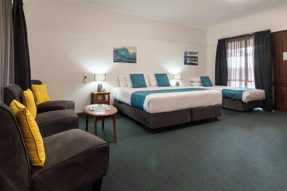 Une chambre d’hôtel avec deux lits, un canapé, une petite table et une vue sur l’océan par la fenêtre.