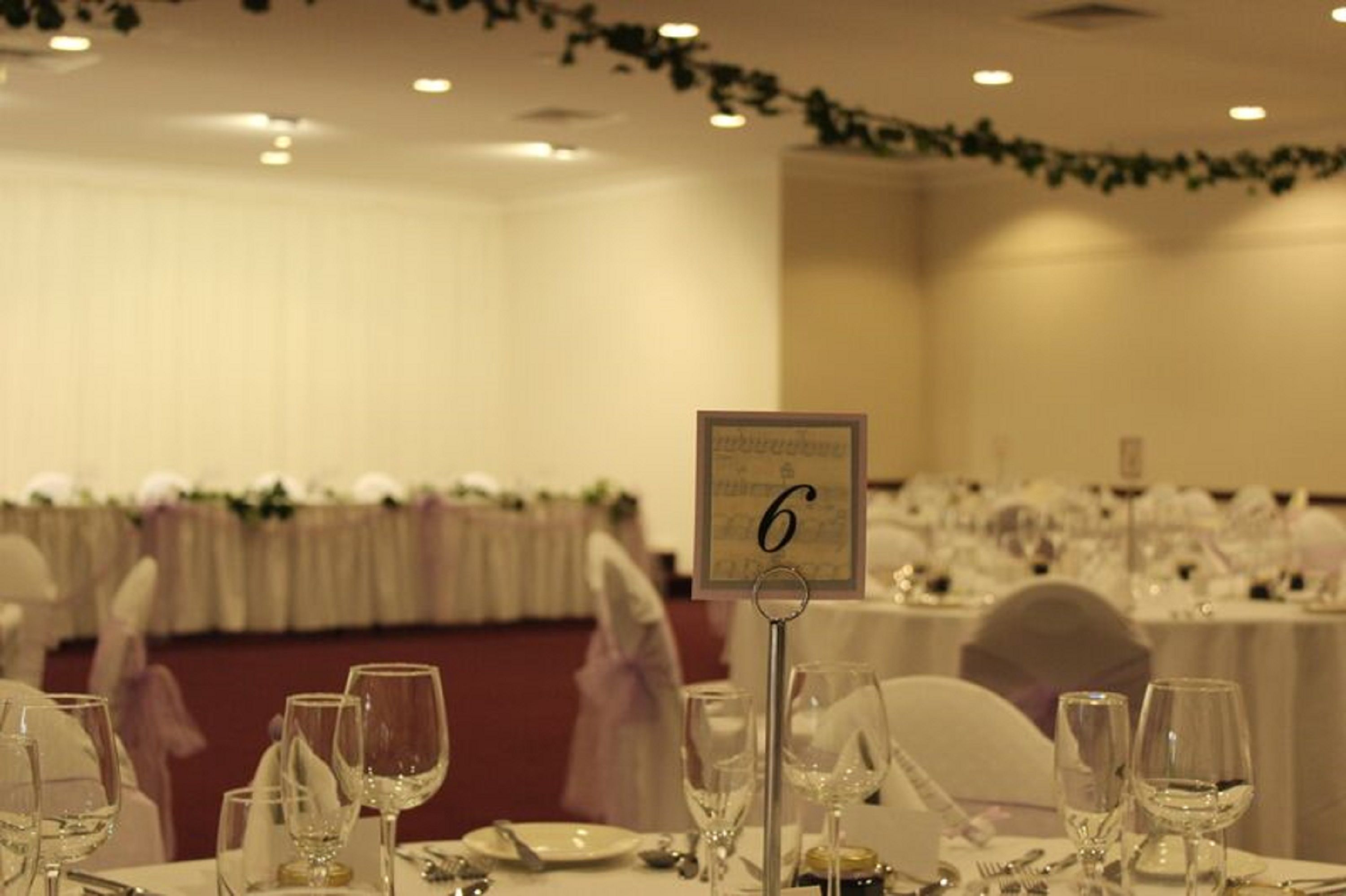 Un salón de banquetes con mesas dispuestas para un evento formal, señalización numérica y una guirnalda floral en el techo.