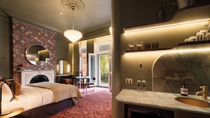 A bedroom with a fireplace, a round mirror, a bed, a desk, and a view of the outdoors. - Medusa Boutique Hotel (Darlinghurst)