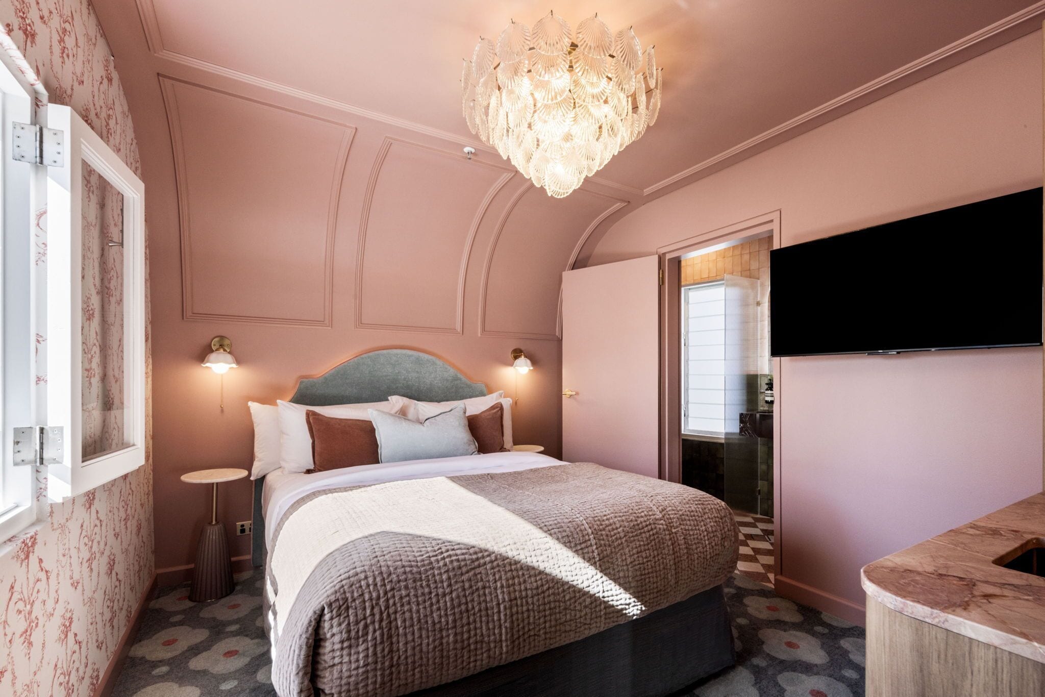 Un dormitorio con una cama grande, un candelabro, un televisor de pantalla plana y la puerta de un baño.