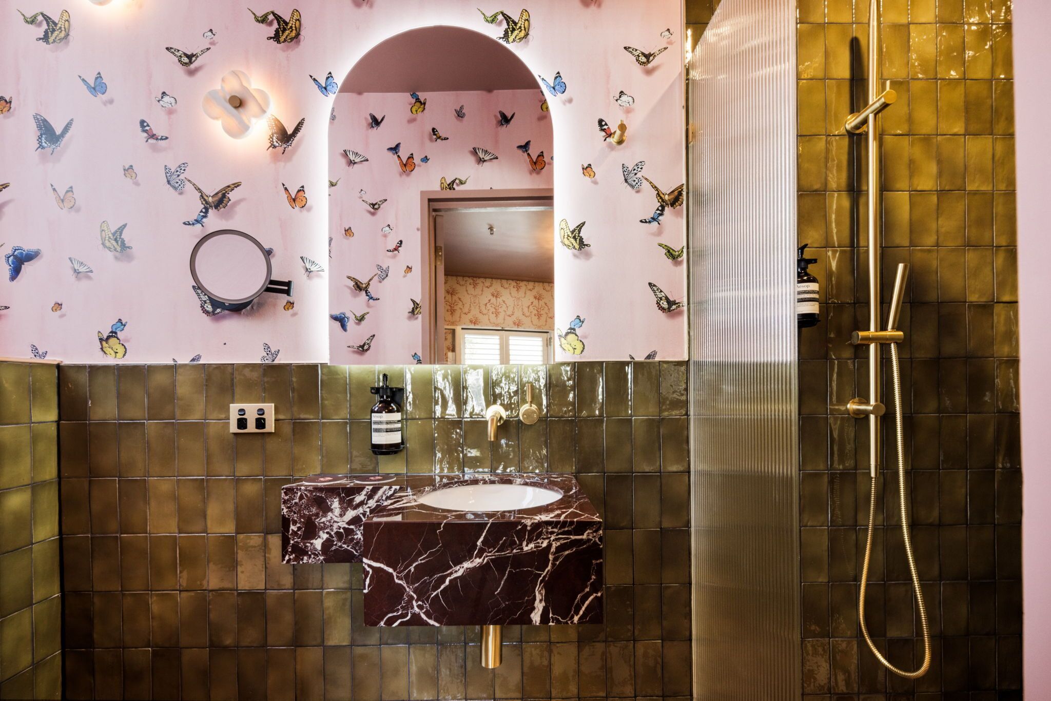 Ein Badezimmer mit Marmorwaschbecken, einer Dusche mit goldener Duschbrause und Schmetterlingsaufklebern an den Wänden.