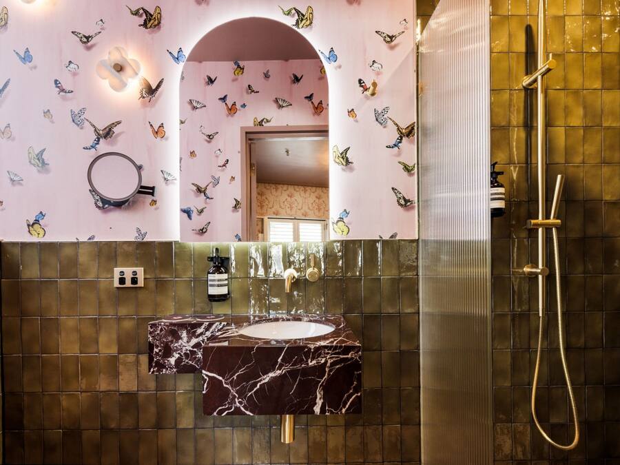 Ein Badezimmer mit Marmorwaschbecken, einer Dusche mit goldener Duschbrause und Schmetterlingsaufklebern an den Wänden.
