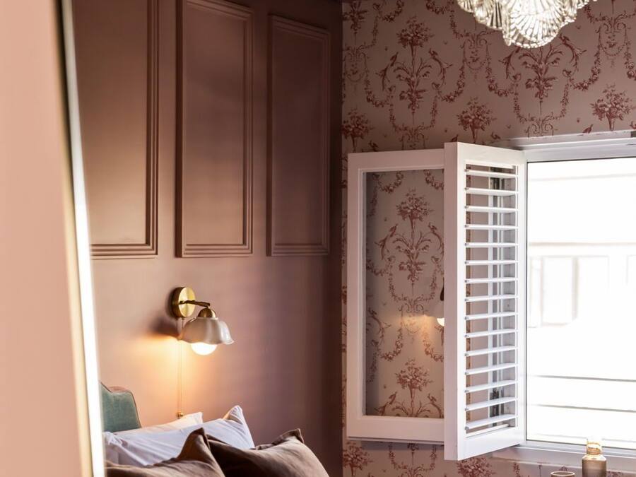 A bedroom with a bed, a wall-mounted lamp, a decorative ceiling light, and a window with blinds.