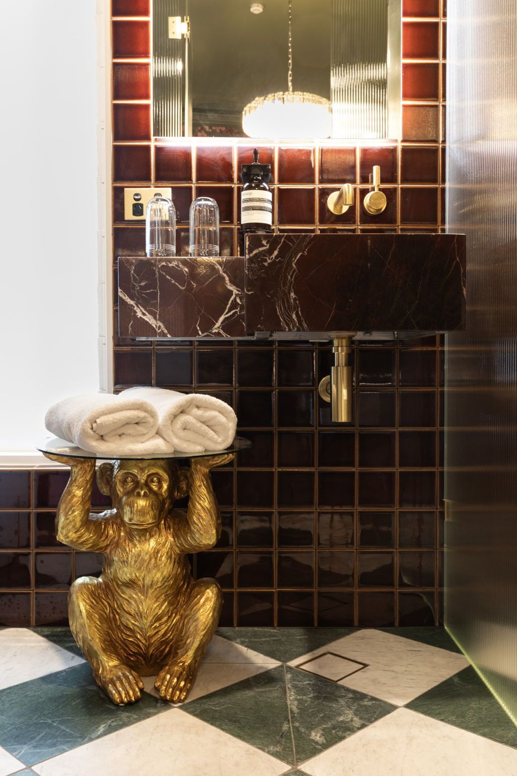 A bathroom with a marble sink, a gold monkey statue holding towels, and a mirror above the sink.