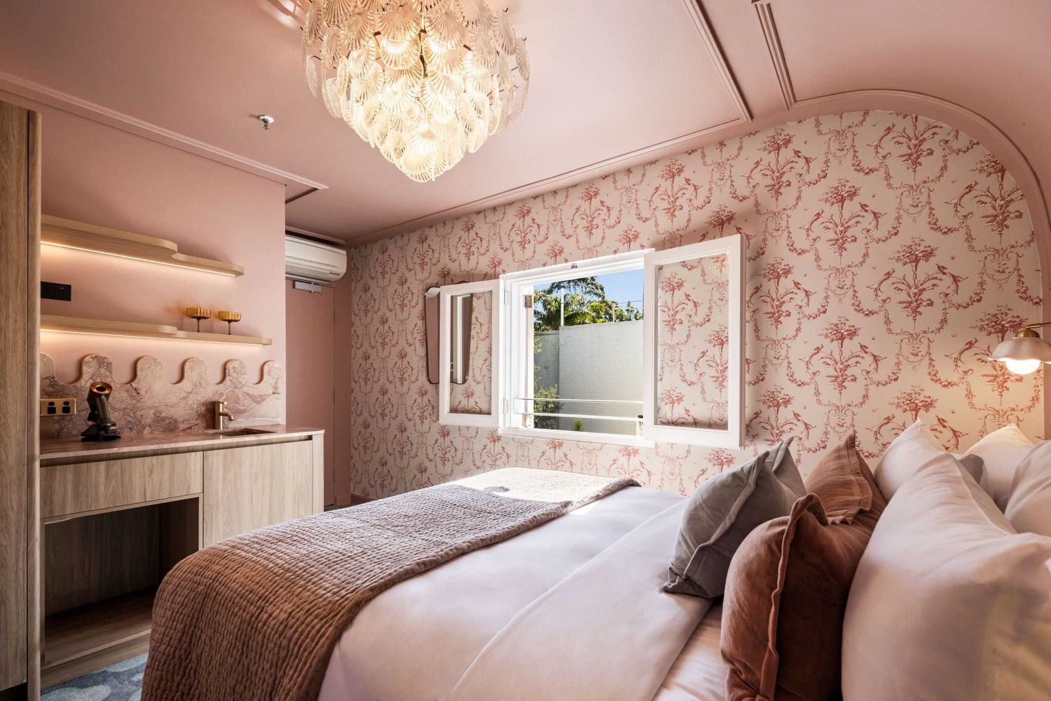 A bedroom with a bed, bedside table, and a window with a view of greenery.