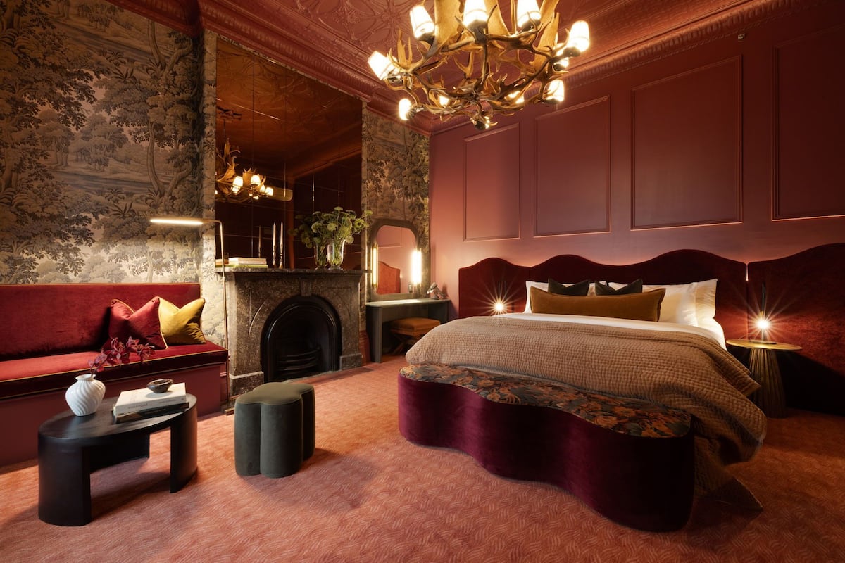 A bedroom with a large bed, a fireplace, a sofa, and a chandelier.