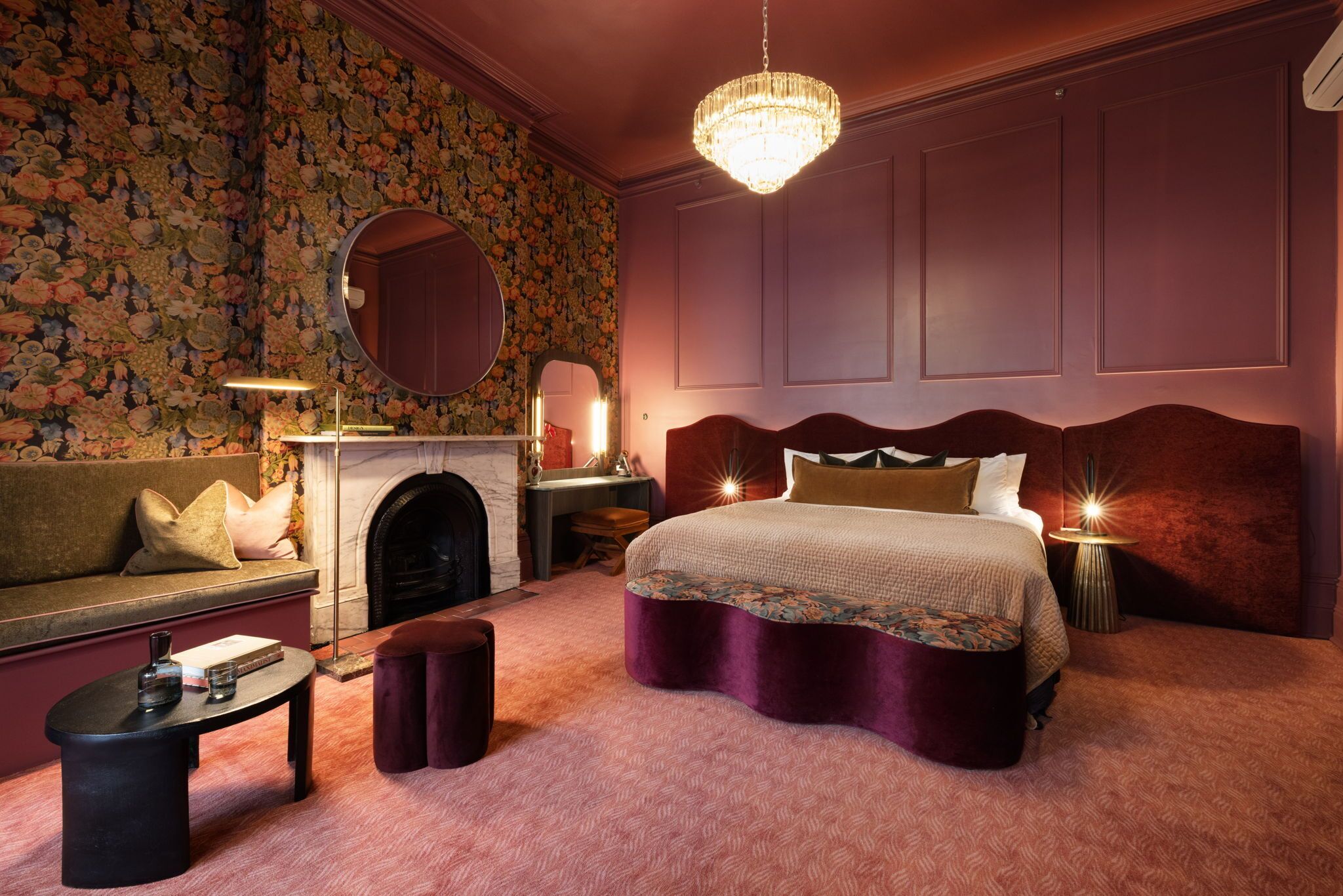 A bedroom with a large bed, a sofa, a fireplace, and a chandelier.