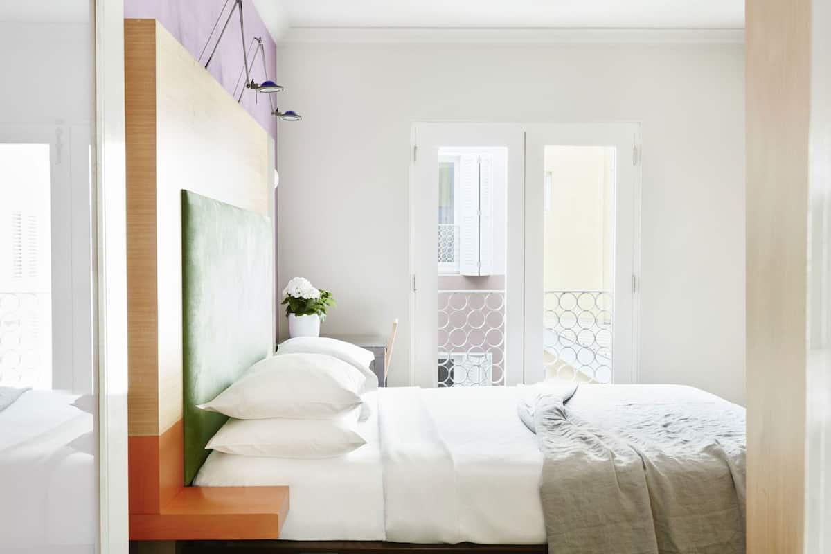 Un dormitorio moderno con cama, mesita de noche, planta en maceta y vistas al balcón.