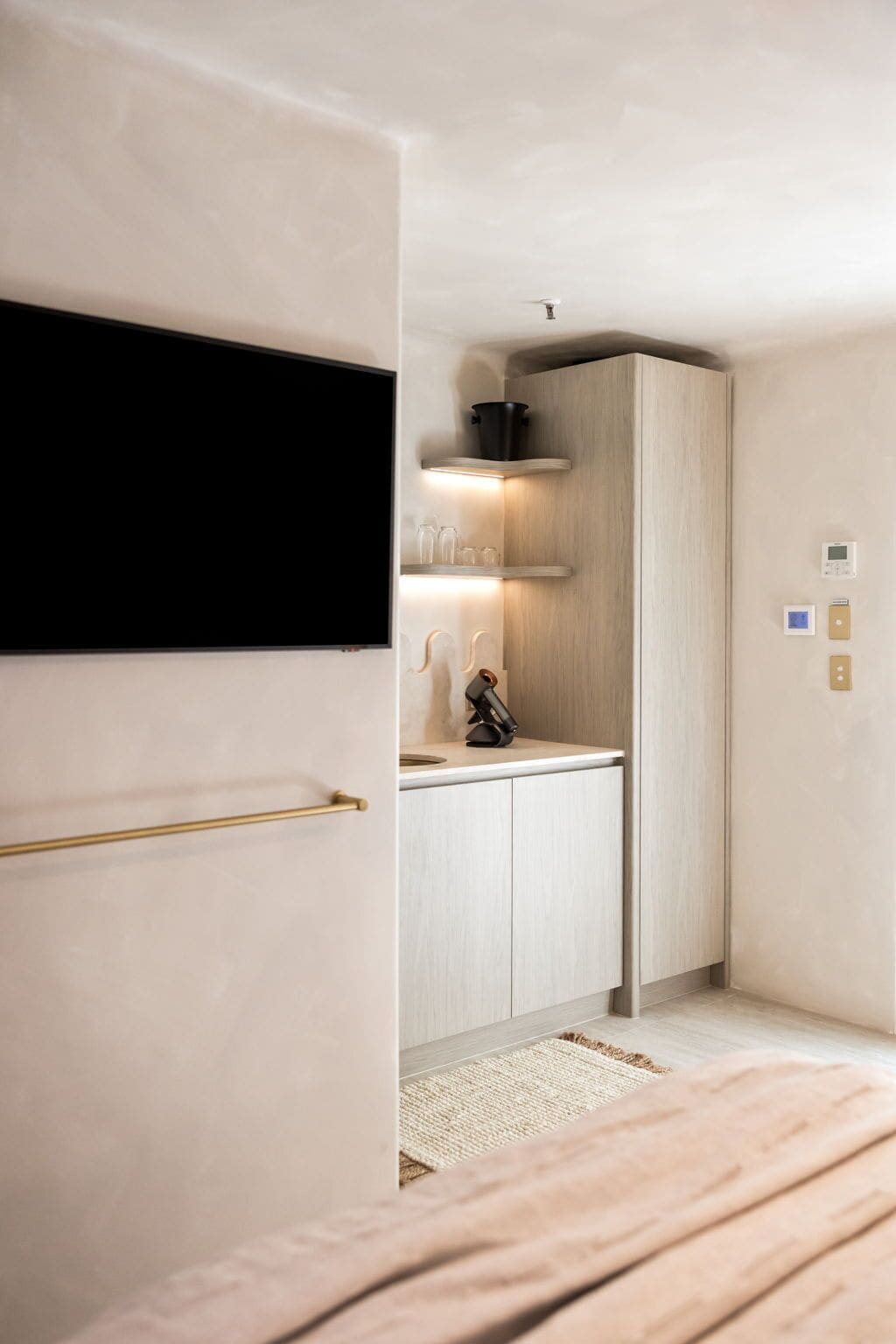 A modern bedroom with a bed, a built-in wardrobe, a small kitchen area with a stove, and a mounted TV.