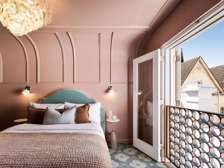 Quarto com cama, um candelabro, mesa de cabeceira e vista para um edifício através de uma porta.