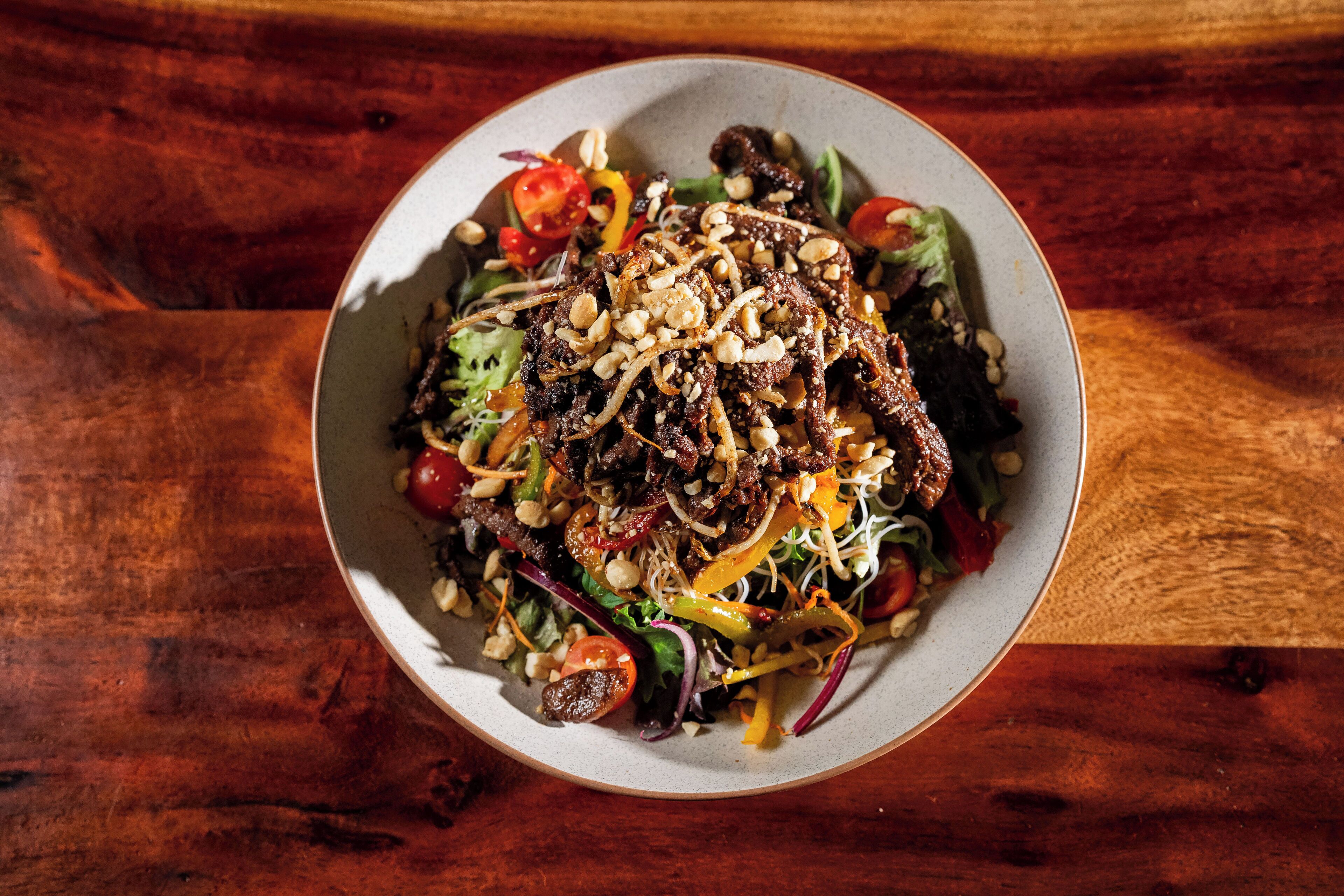 A bowl of salad with various vegetables and nuts on a wooden table.