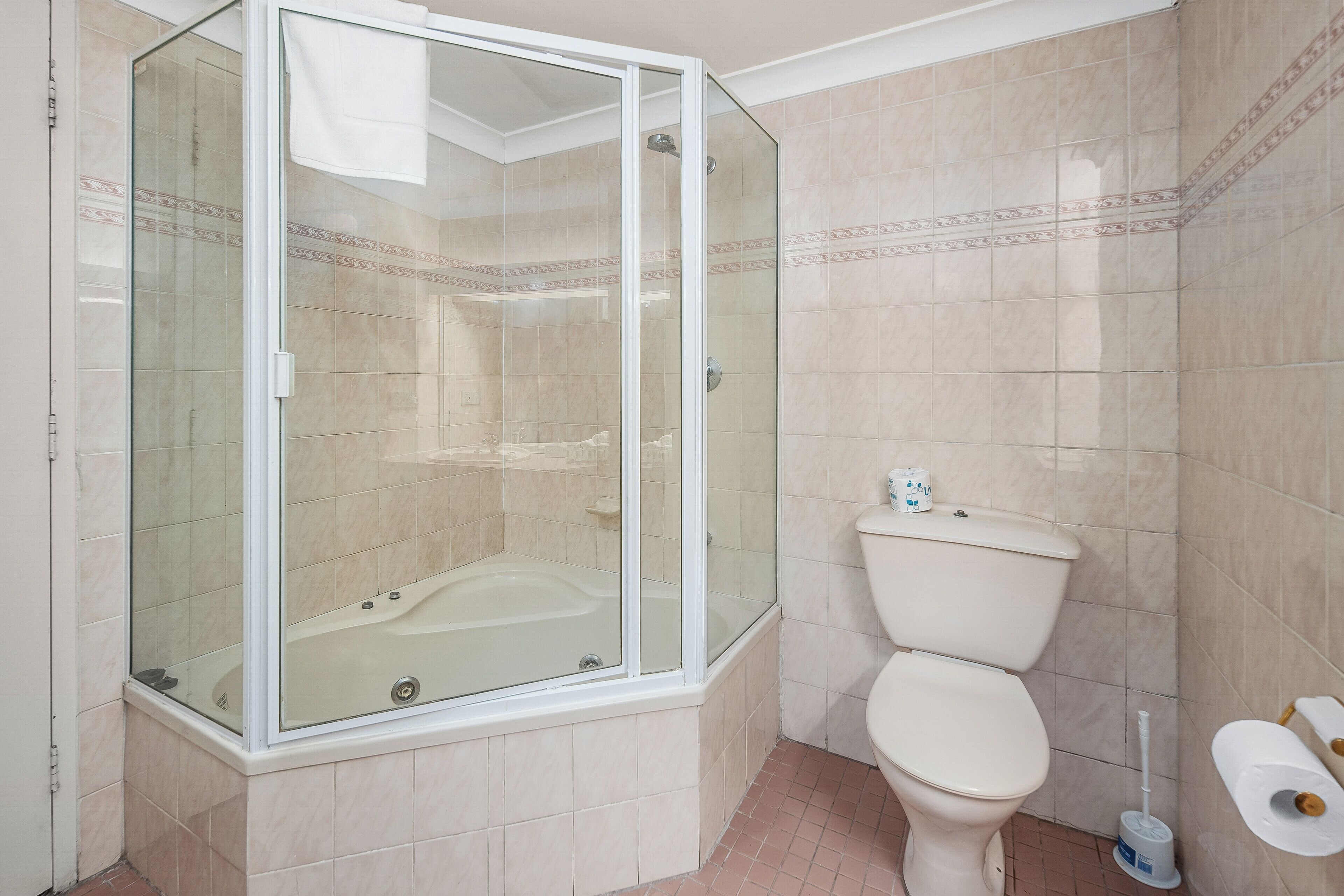 Une salle de bain avec une douche à parois de verre, des toilettes et un rouleau de papier toilette accroché au mur.
