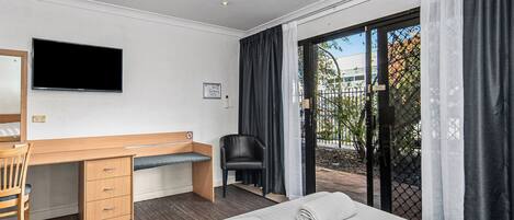 A hotel room with a bed, a desk with a chair, a TV mounted on the wall, and a view of the outside through a glass door.