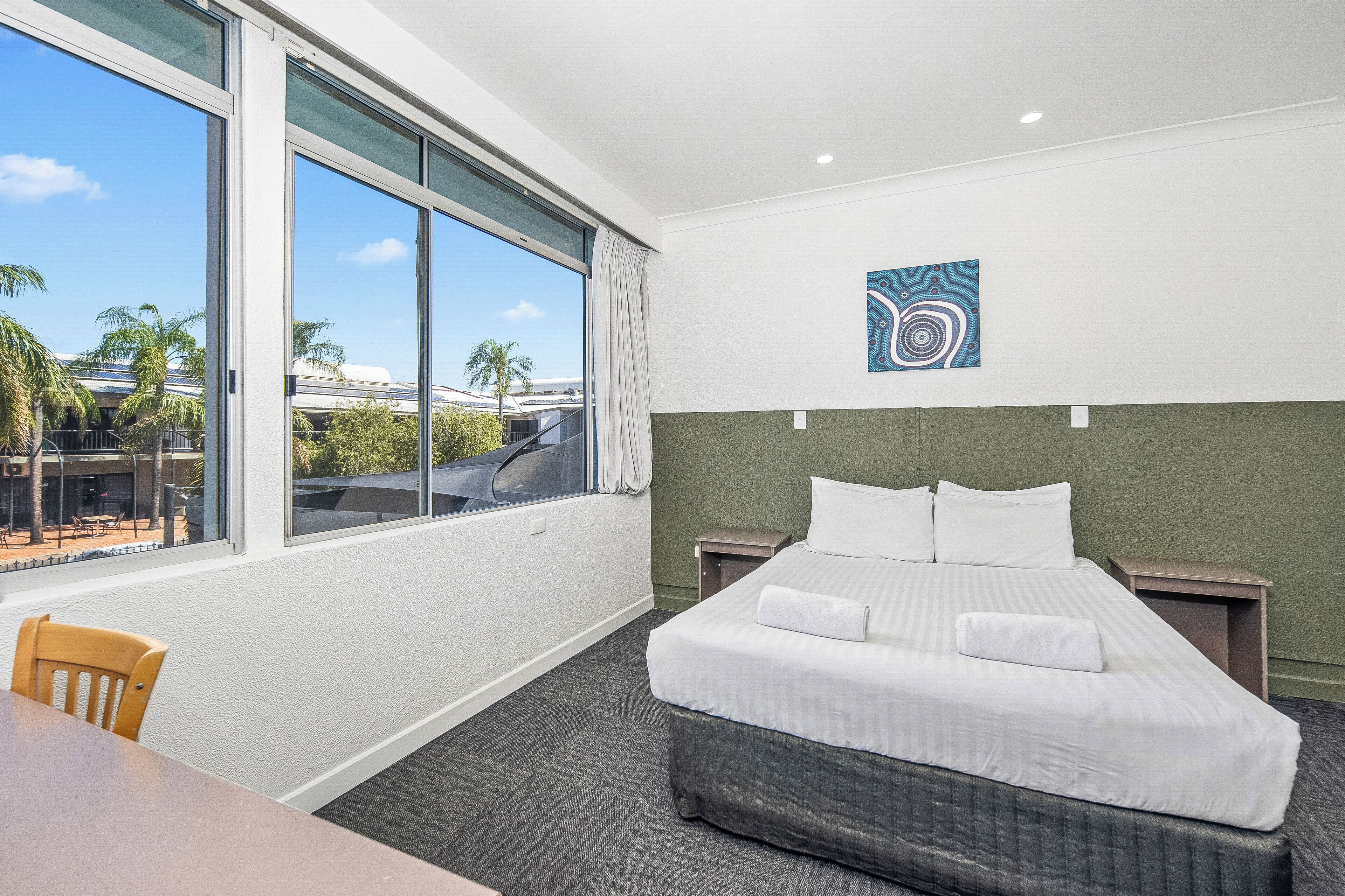 A hotel room with a large window, a bed, a chair, and a small table.