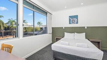 A hotel room with a large window, a bed, a chair, and a small table.