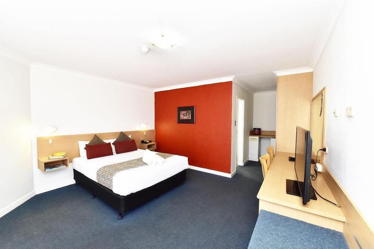 Ein Hotelzimmer mit Bett, Nachttisch, Lampe, Fernseher und einer roten Akzentwand.