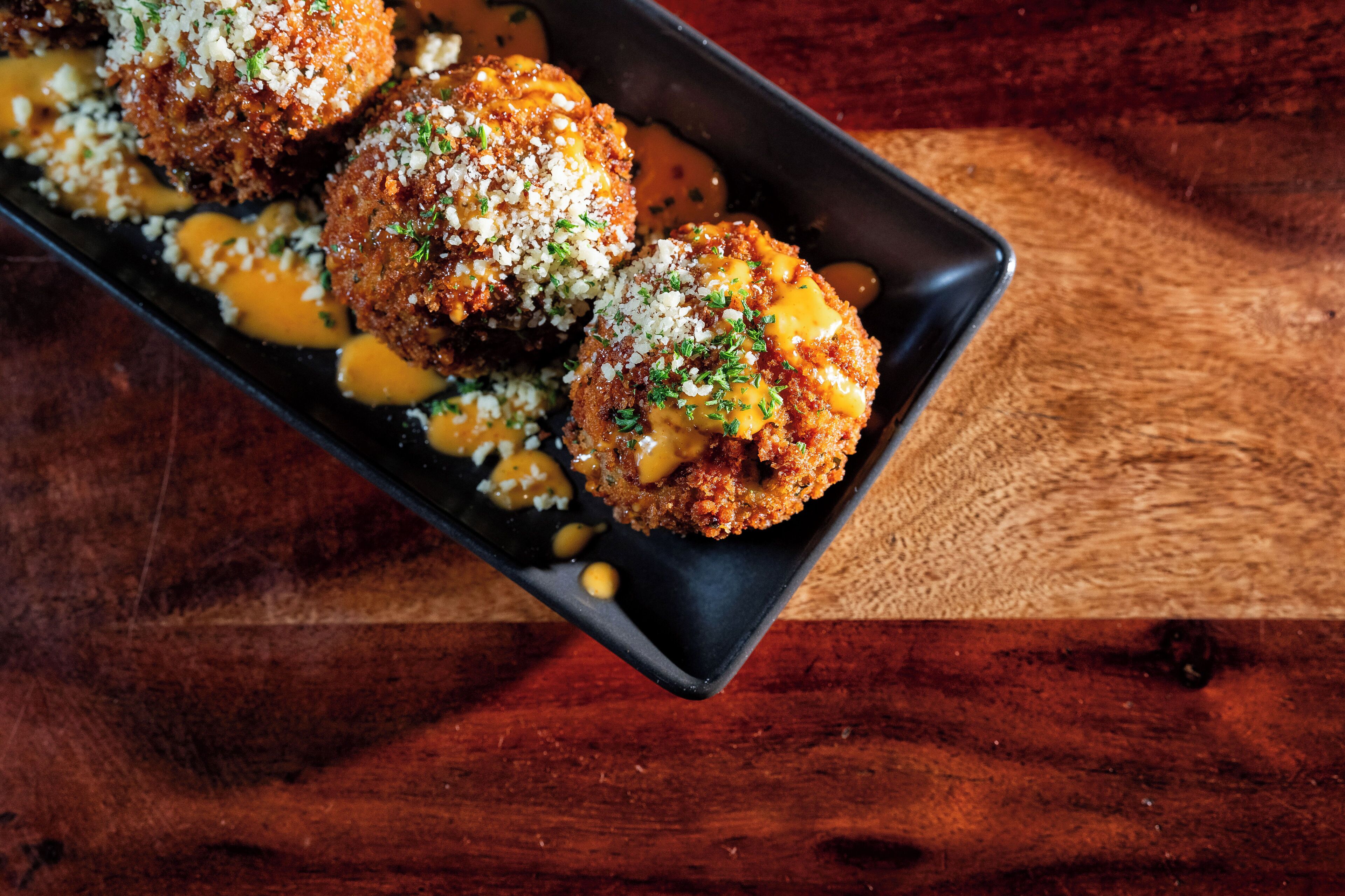A tray of food with breaded balls, cheese sauce, and grated cheese.