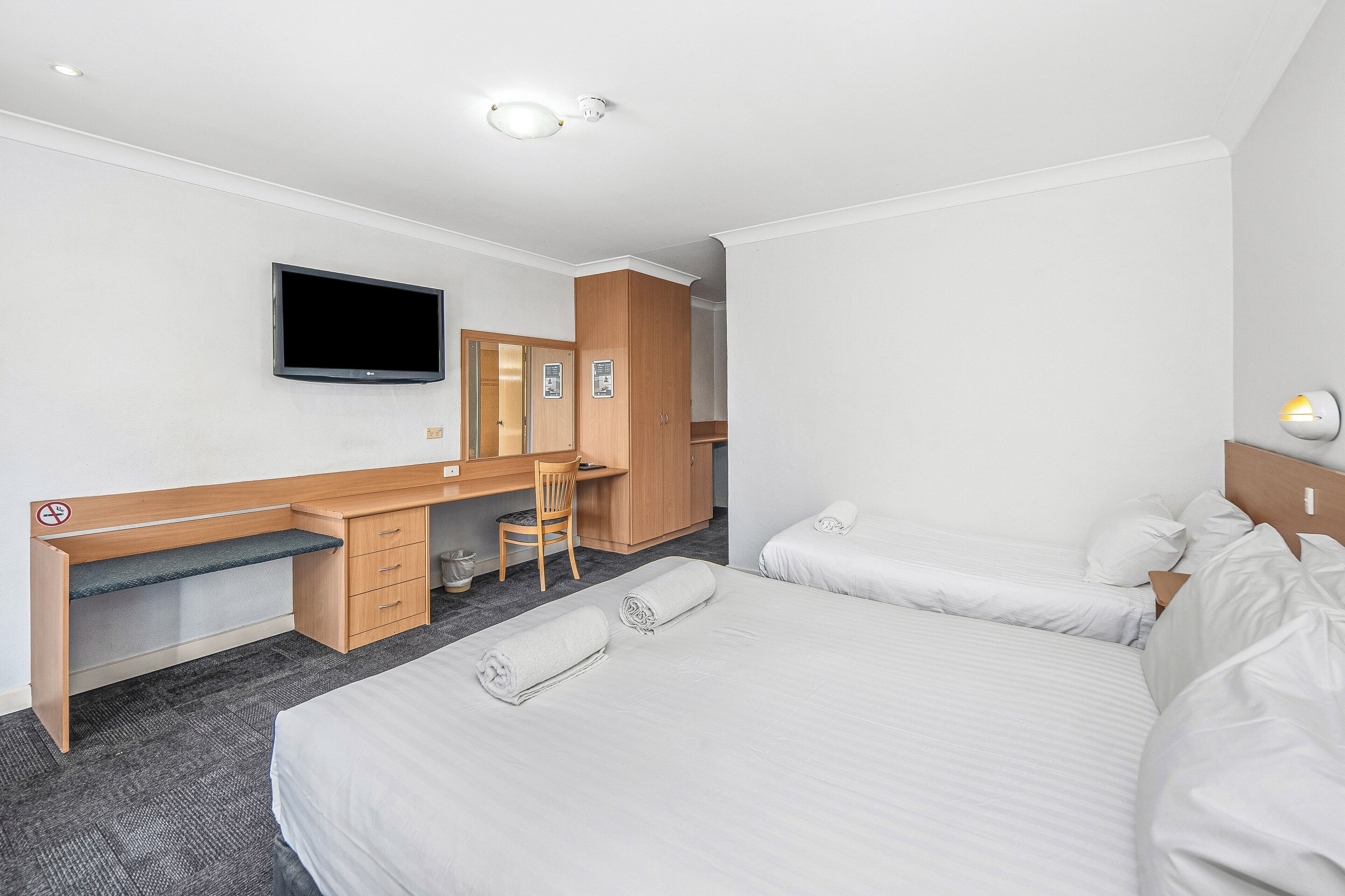 A hotel room with a bed, a desk, a chair, a television, and a wardrobe.
