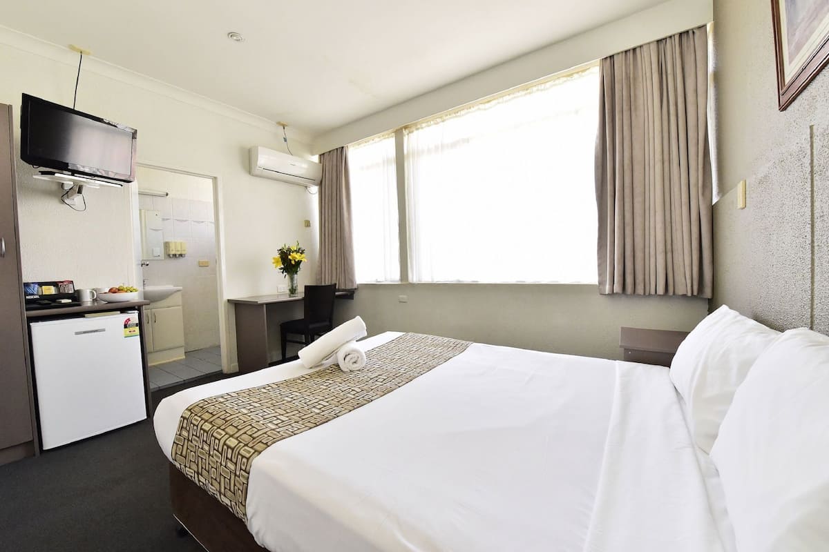 A hotel room with a bed, a desk with a computer, a TV, and an air conditioning unit.