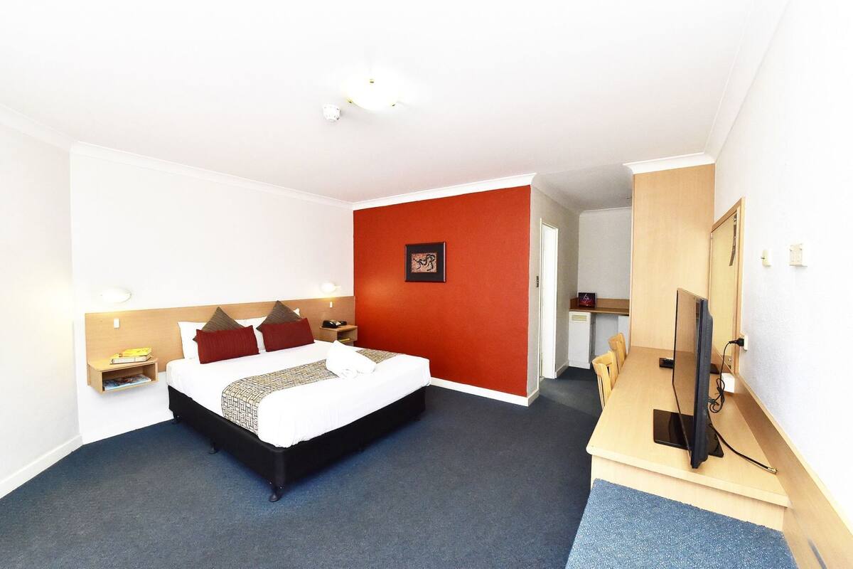 A hotel room with a bed, bedside tables, a desk with a computer, and a television.