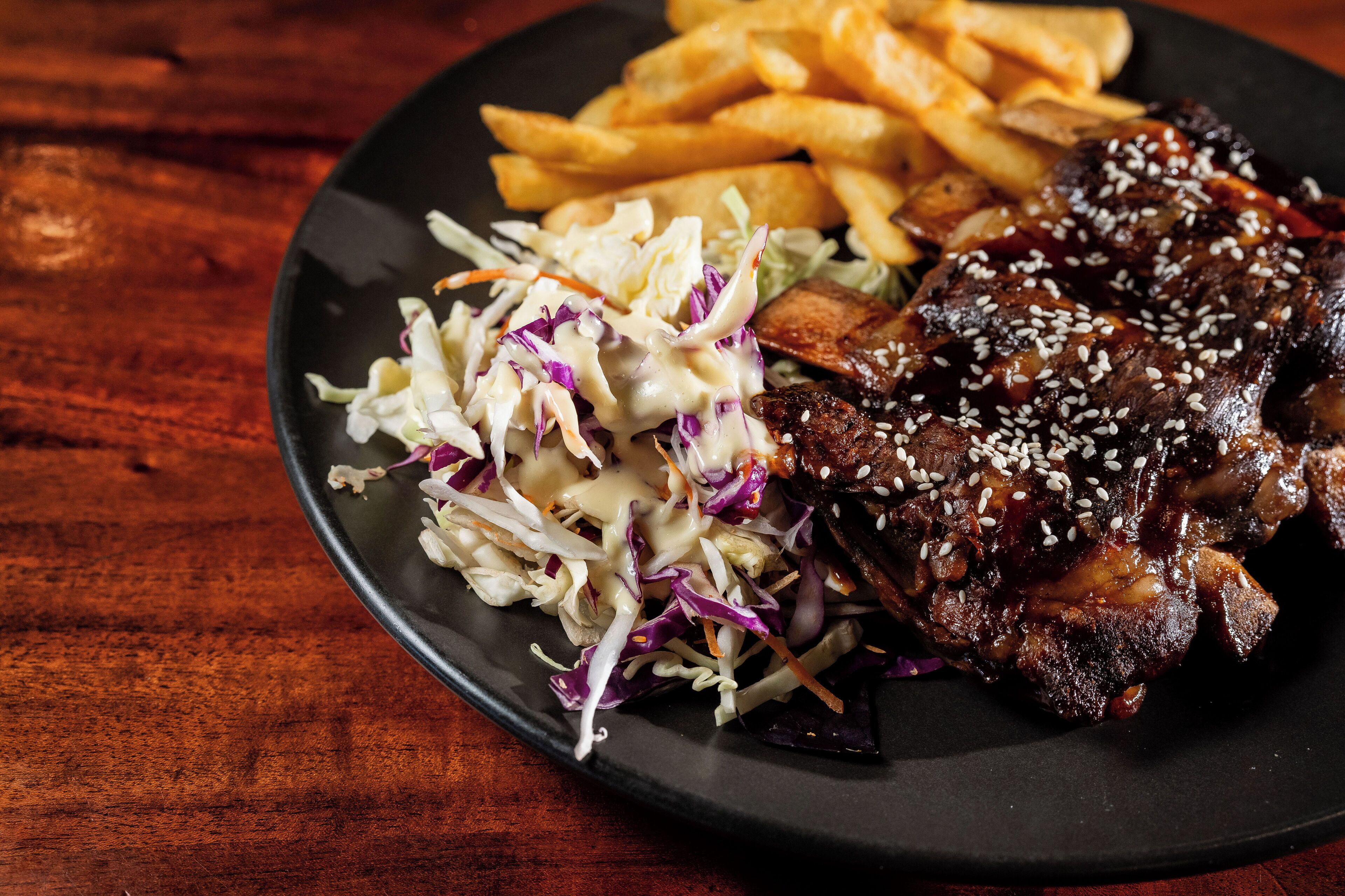 A plate with ribs, French fries, and coleslaw.
