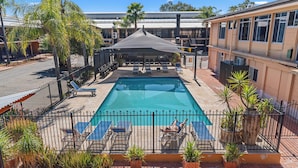 A swimming pool with lounge chairs, surrounded by a fence and potted plants.