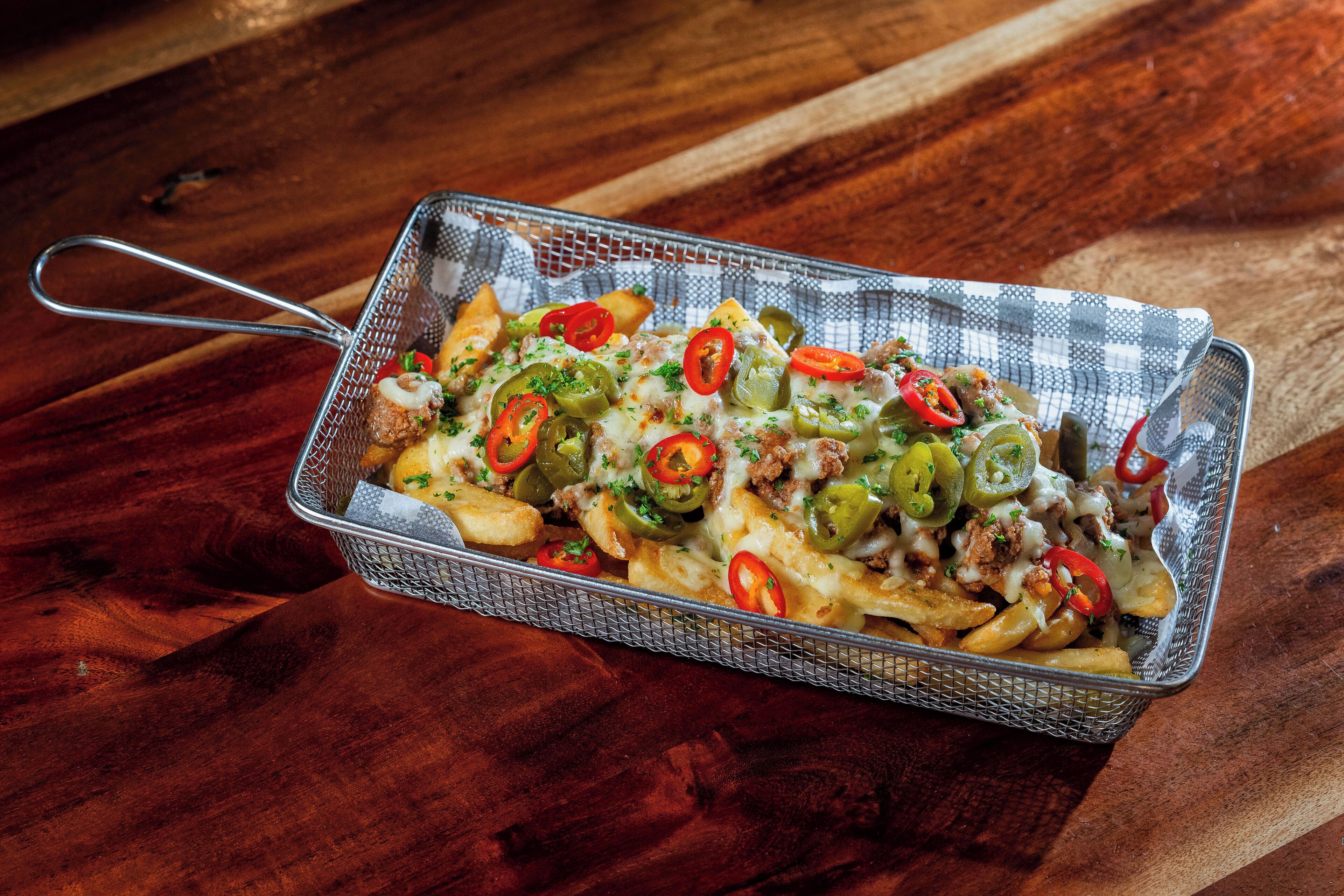 Una bandeja de nachos con queso, jalapeños y carne sobre una mesa de madera.