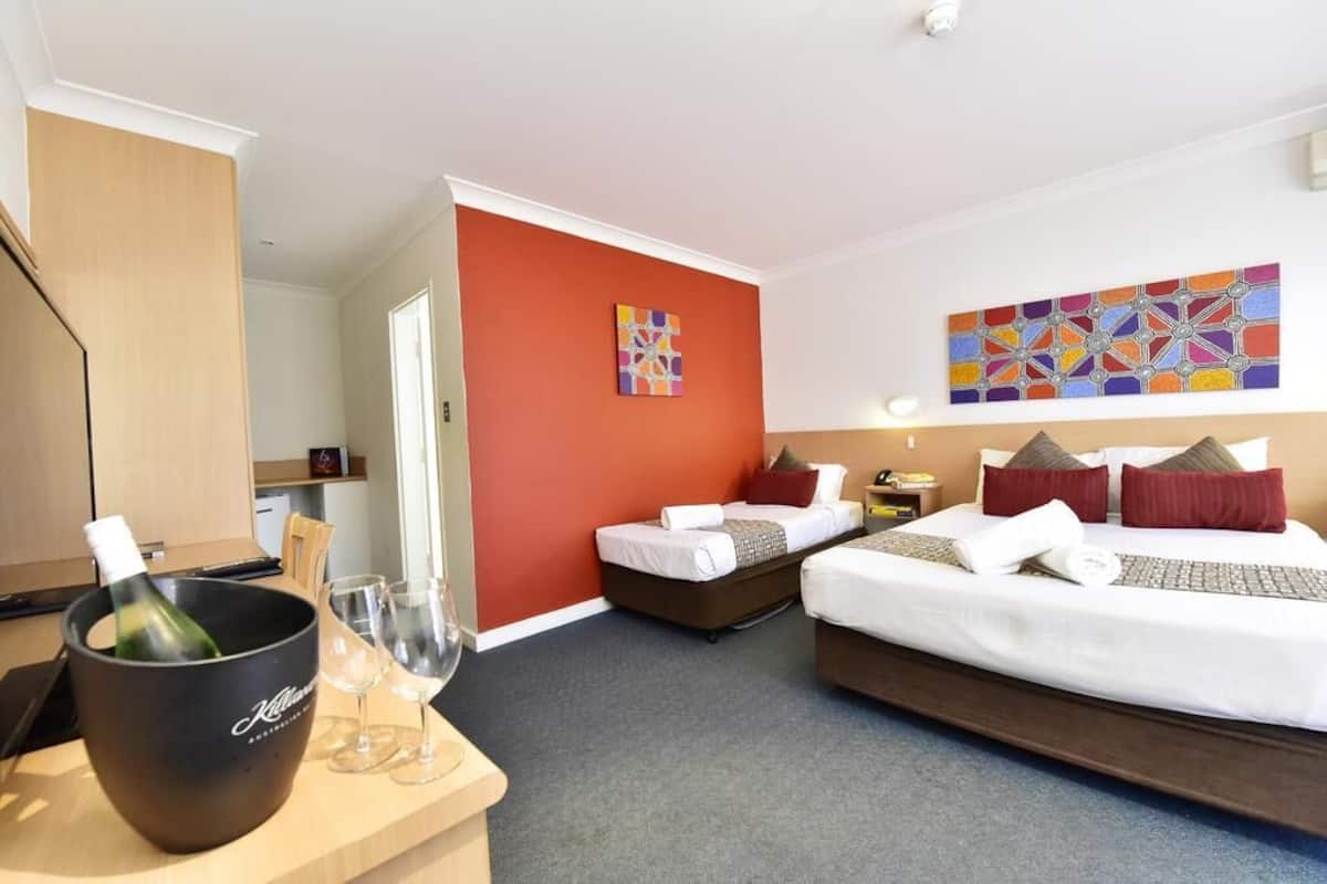 Ein Hotelzimmer mit zwei Betten, einer Minibar und einer Essecke mit einer Weinflasche.