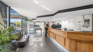 A modern hotel lobby with a reception desk, seating area, and a view of the outside.