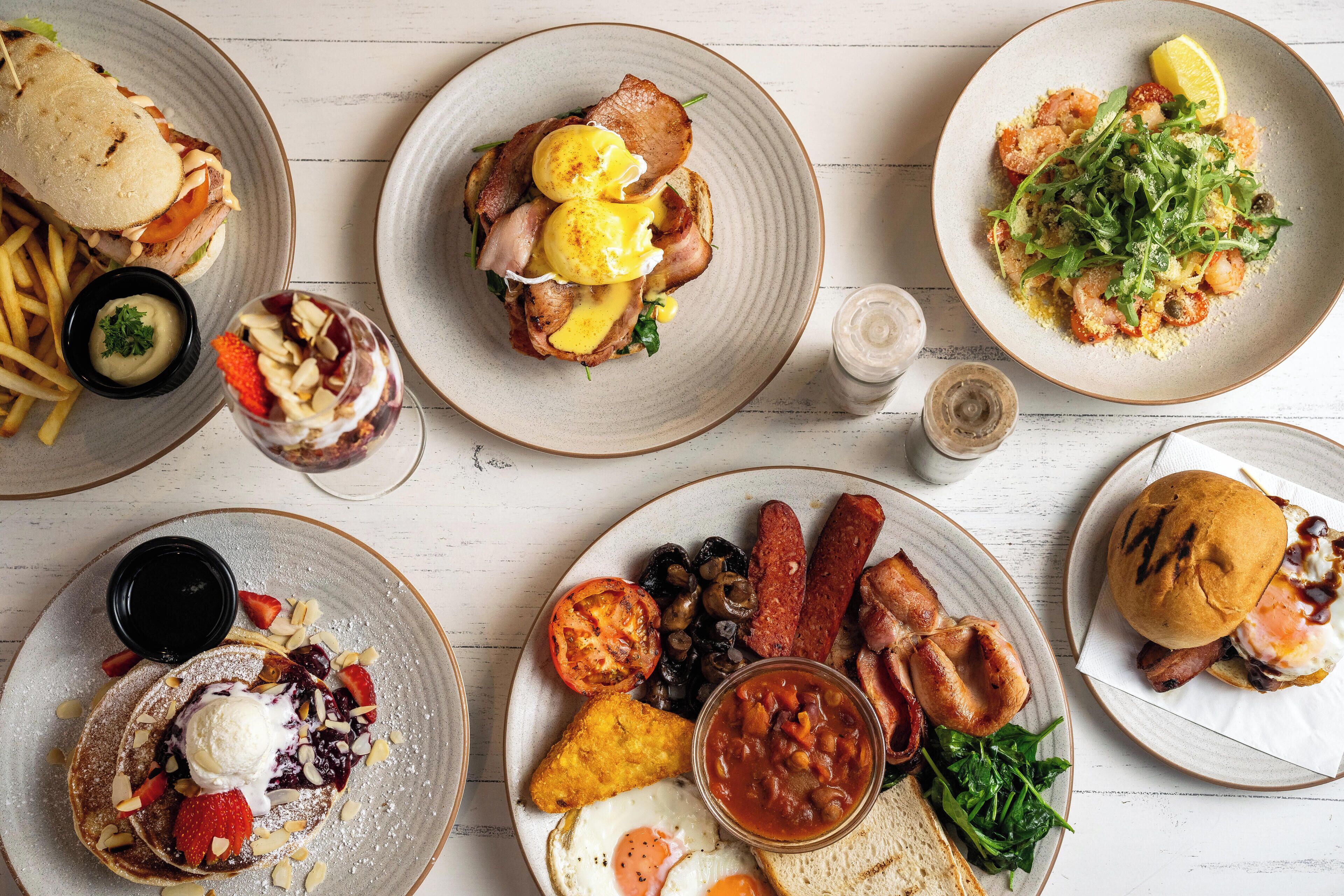 Une variété de plats pour le petit-déjeuner sont présentés sur des assiettes, notamment des œufs, du bacon et des toasts.
