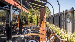 An outdoor seating area with tables and chairs, a pergola, and a metal fence.