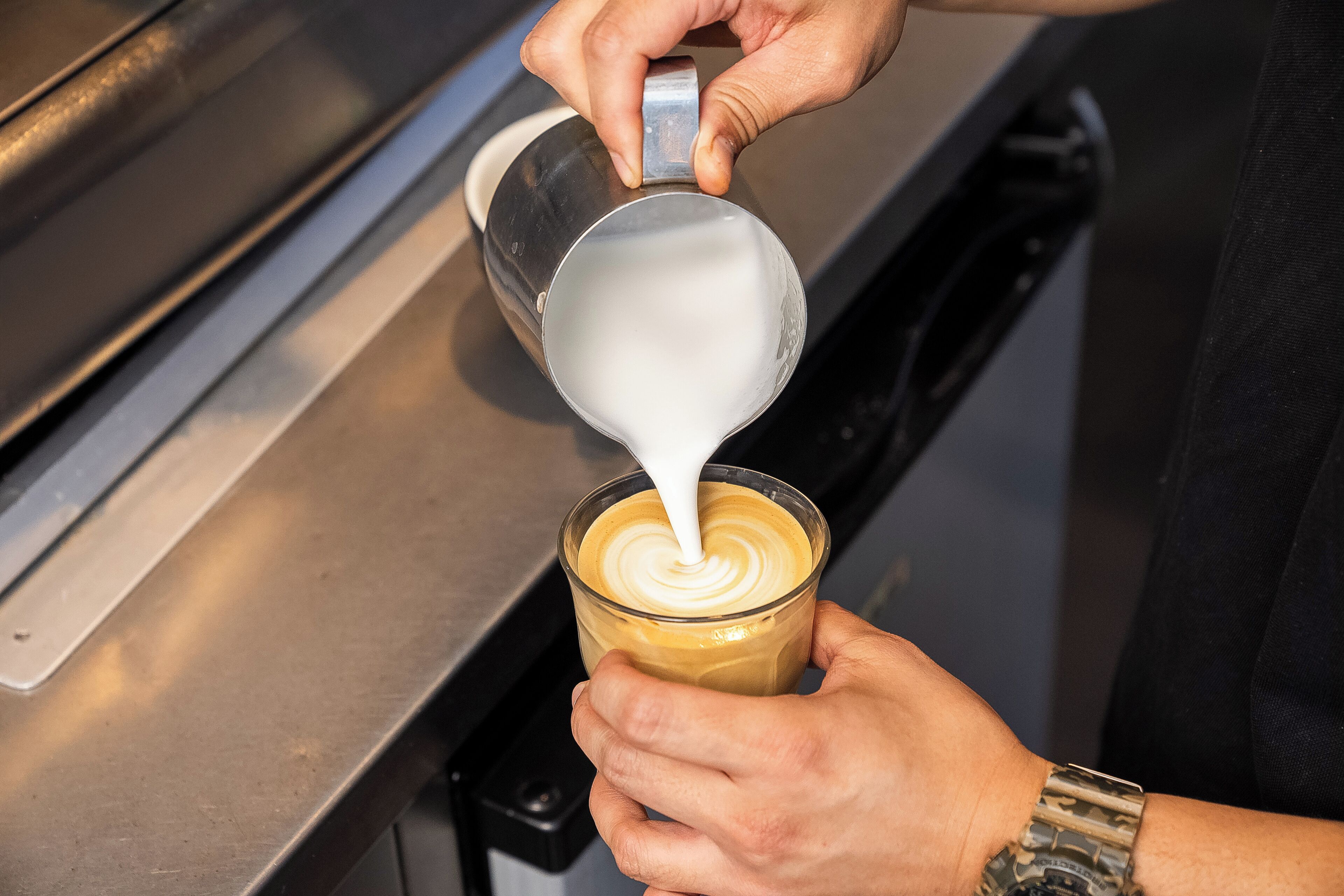 Una persona vertiendo leche en una taza de café, creando un diseño decorativo con latte.