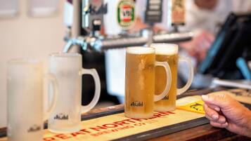 Una barra con varios vasos de cerveza, una mano y una grifería de fondo.