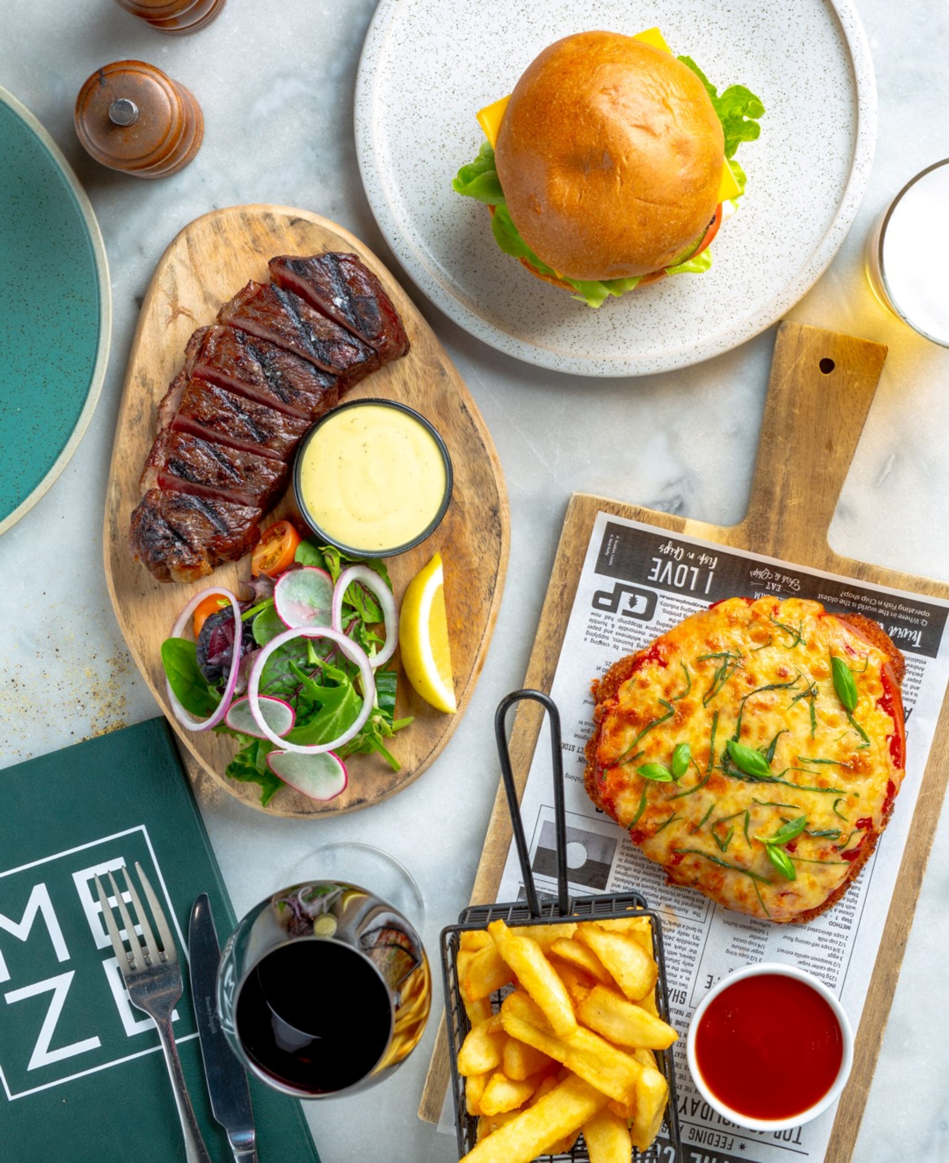 A meal with a steak, burger, and fish patty, accompanied by fries and salad.