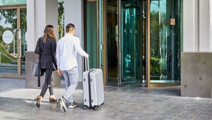 Un hombre y una mujer caminando hacia una puerta giratoria con una maleta.