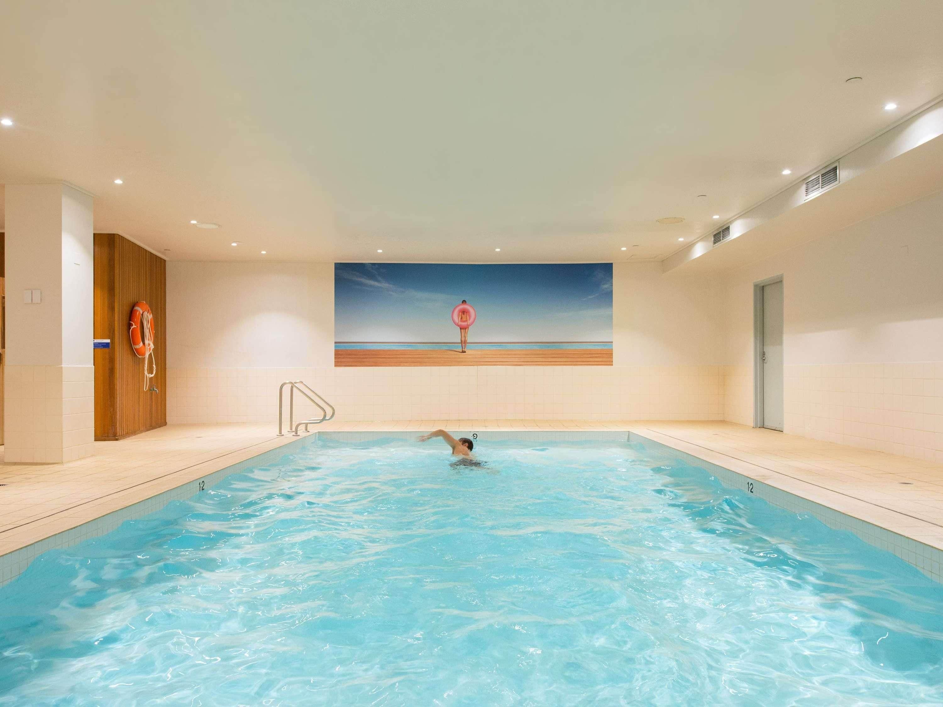 Una piscina interior con un flotador salvavidas, una pared de madera y un cuadro que representa una playa.