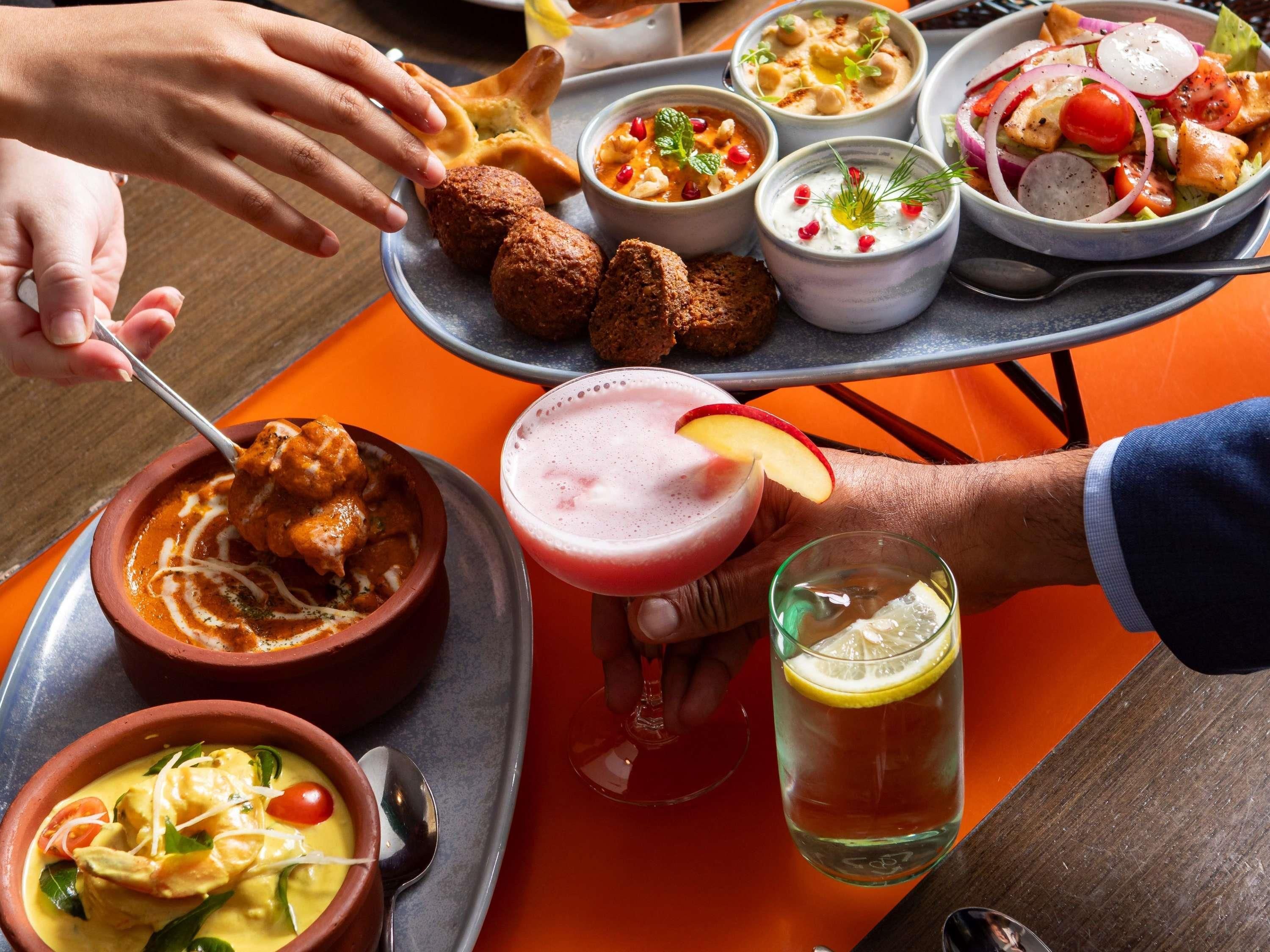 A variety of dishes and drinks on a tray, including a bowl of soup, a plate of falafel, and a glass of iced beverage.