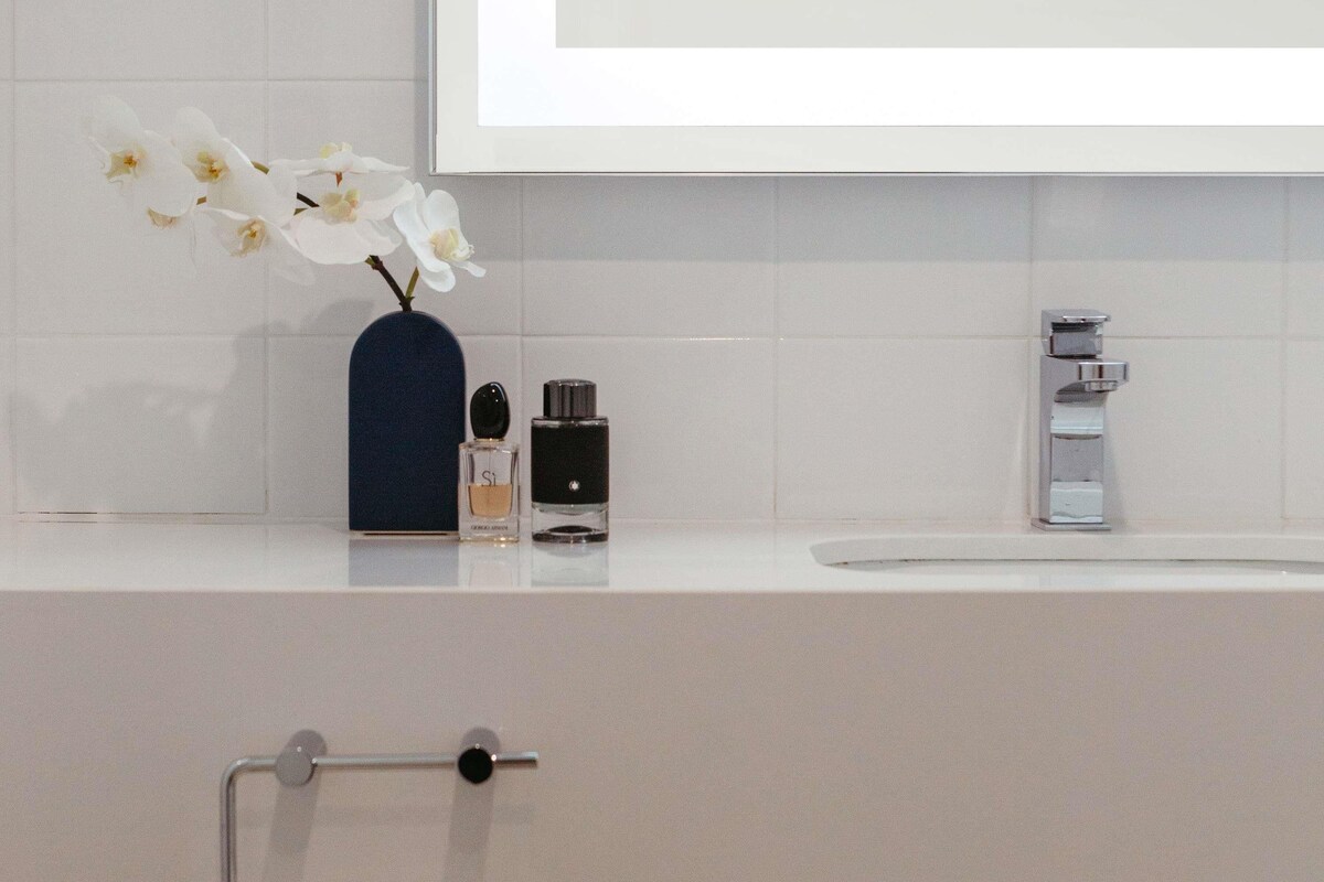 A bathroom with a white sink, a blue vase with white flowers, and two bottles of perfume.