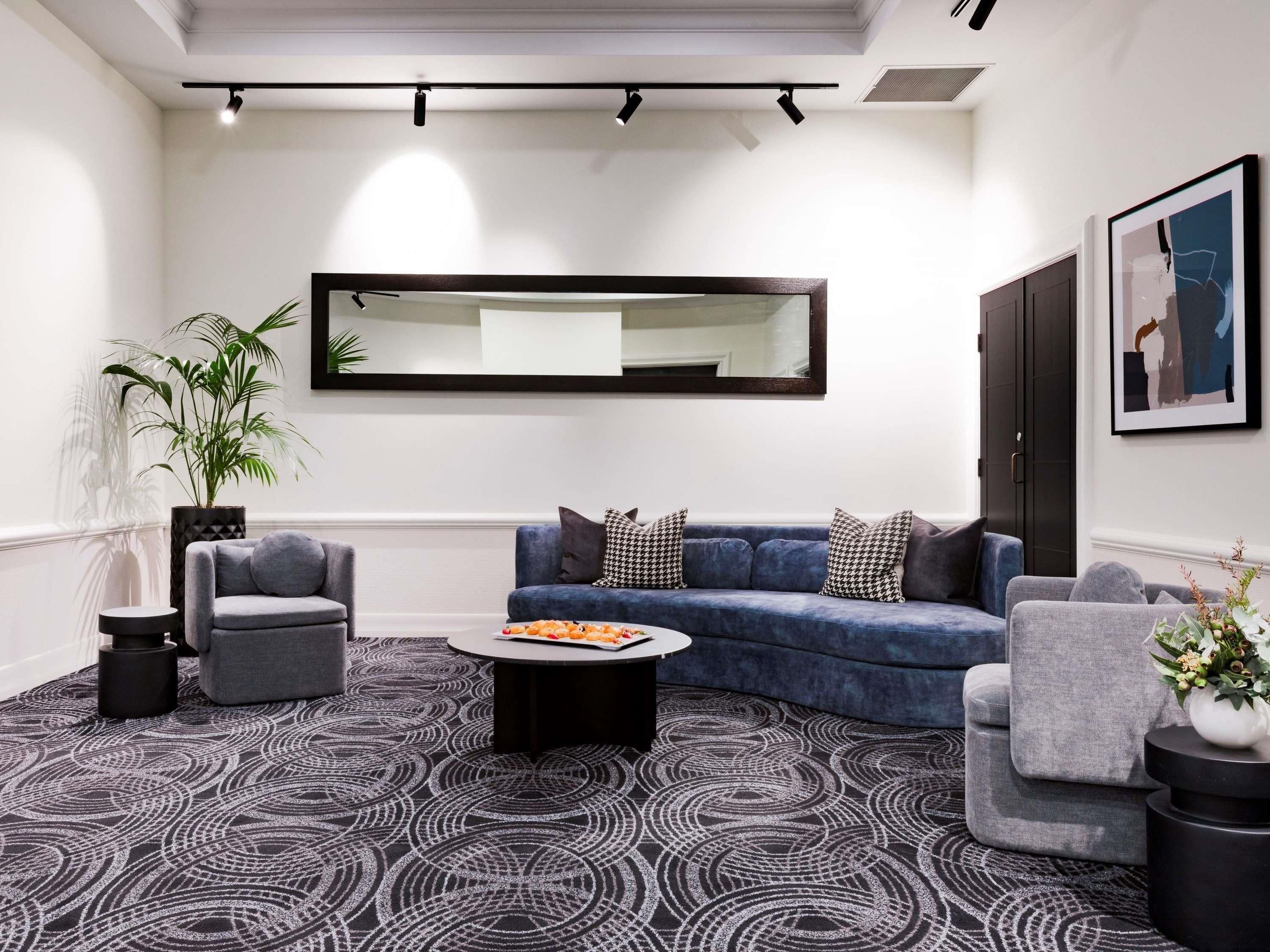 A modern living room with a blue sofa, grey armchairs, a coffee table, and a large mirror on the wall.