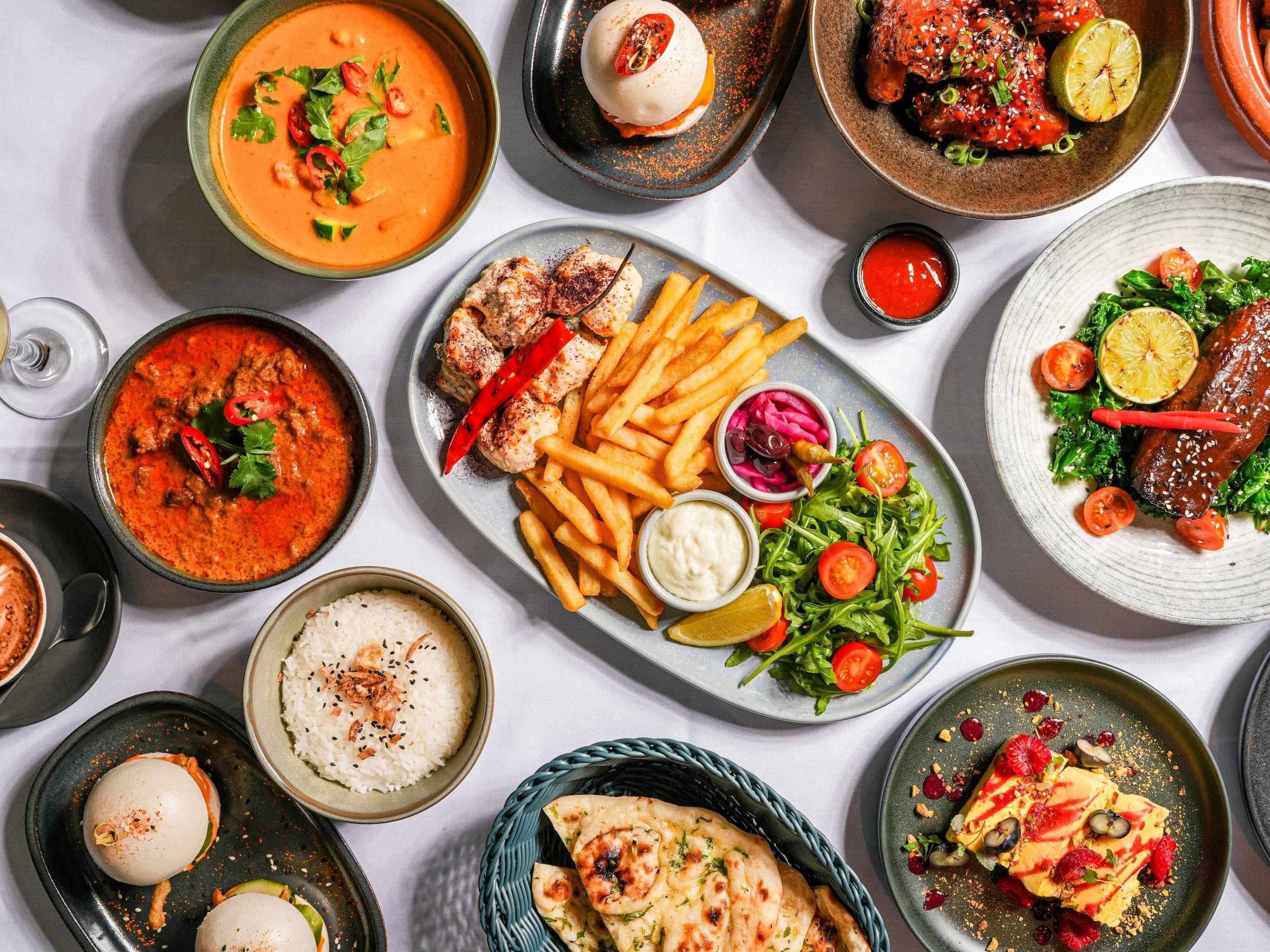 A variety of dishes including a bowl of soup, grilled meat, French fries, a salad, and rice.